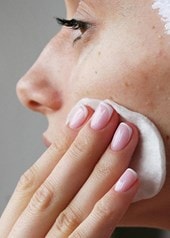 Nahaufnahme einer Person die mit einem Wattepad die Wange reinigt Hautpflege gegen Unreinheiten