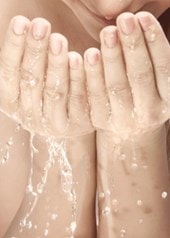 Frau mit langen Haaren wäscht sich das Gesicht mit Wasser