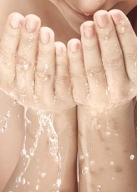 Frau mit langen Haaren wäscht sich das Gesicht mit Wasser