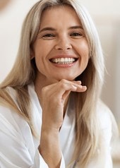 Lächelnde blonde Frau in weisser Bluse mit Hand am Kinn, Porträt in hellem Innenraum