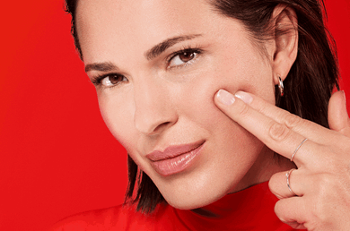 Frau mittleren Alters mit einem sanften Lächeln berührt ihre linke Wange