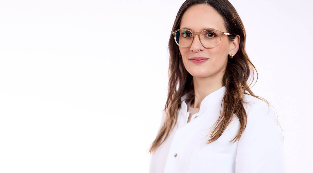 Hautärztin Dr. med. Schaaf trägt Brille und weißen Kittel und blickt sympathisch in die Kamera