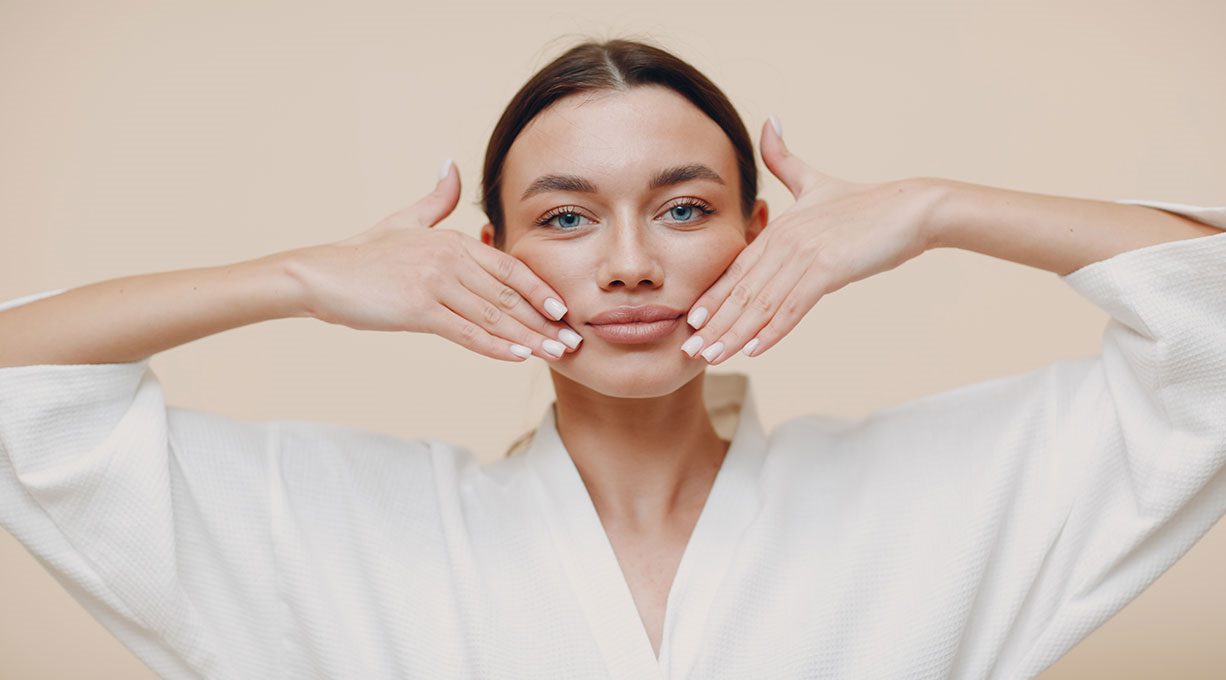Junge Frau macht Massagebewegung im Gesicht als Teil eines Gesichtsyoga-Trainings