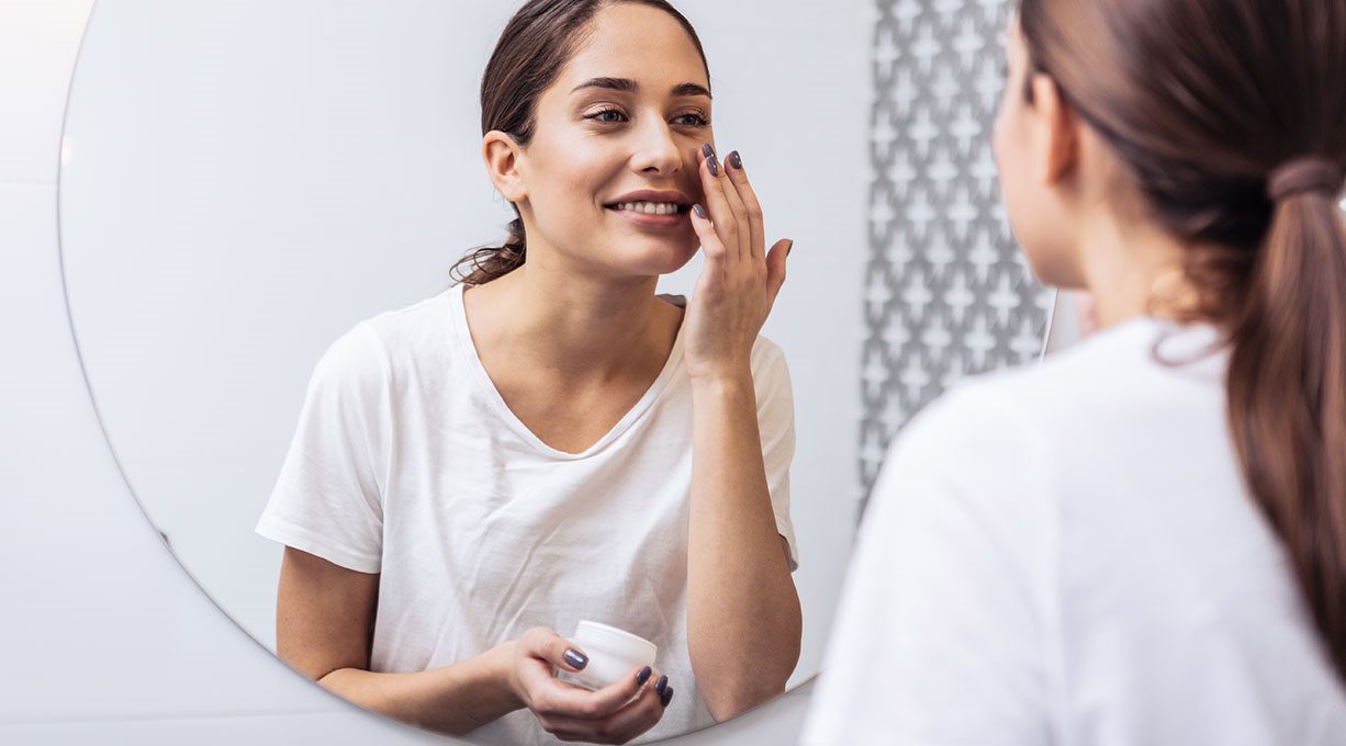 Eine junge Frau pflegt ihre Haut mit Resveratrol-Creme vor dem Spiegel