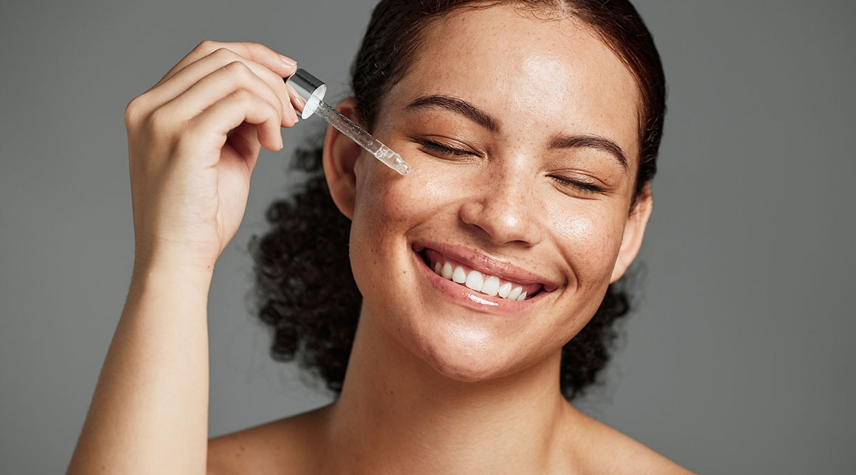 Lächelnde Frau nutzt Serum, um ihre Haut mit Feuchtigkeit zu versorgen.