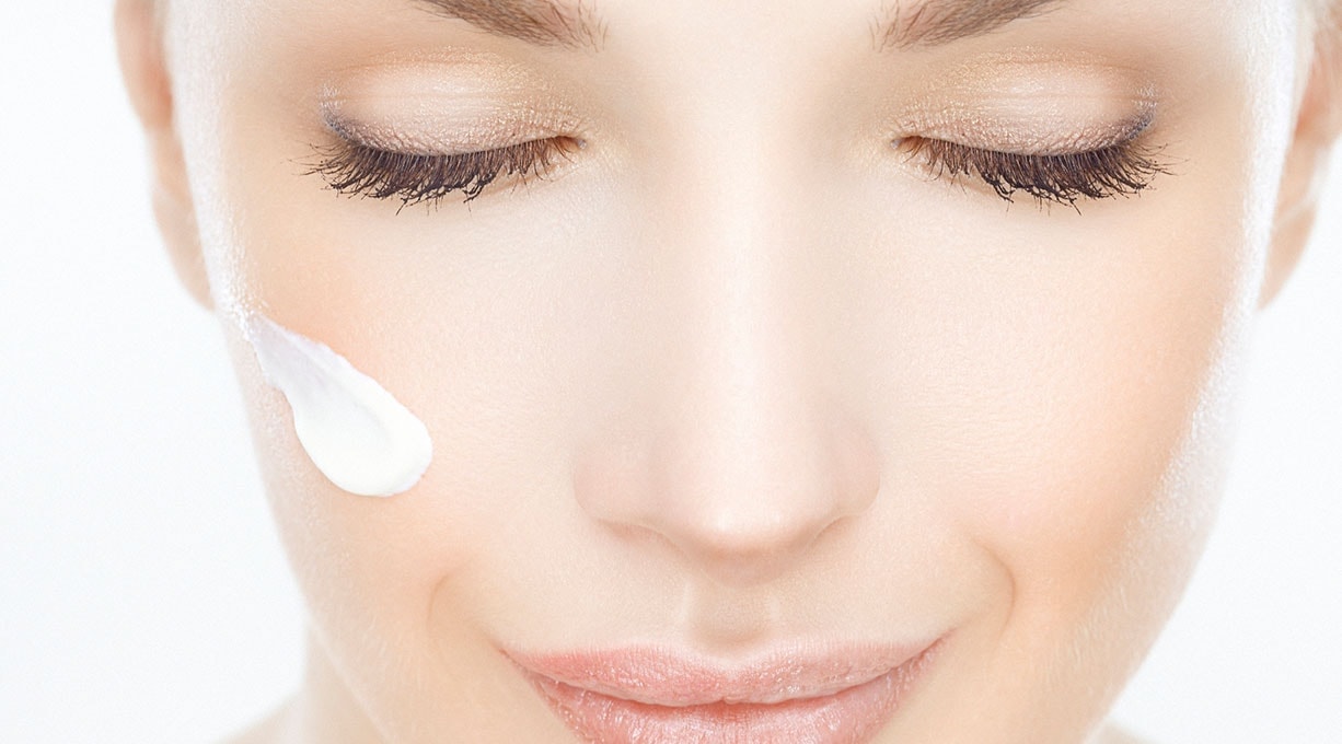 Nahaufnahme einer Frau mit geschlossenen Augen, die sanfte Creme aufträgt.