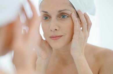 Frau prüft im Spiegel ihre Haut nach der Anwendung einer Anti-Aging-Creme.