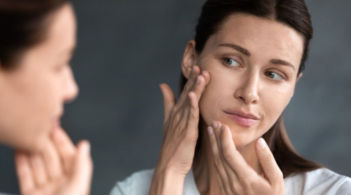 Frau betrachtet kritisch ihr Gesicht im Spiegel und prüft ihre Hautstruktur.