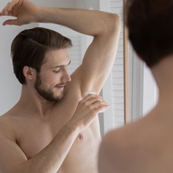 Junger Mann pflegt seine Achseln mit einem Deo Roll-on, um Frische und Schutz vor Schweißgeruch zu bewahren.