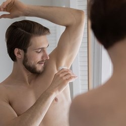Homme appliquant un déodorant roll-on pour réduire la transpiration et éviter les odeurs corporelles.
