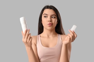 Nachdenkliche Frau hält Spray und Deo-Stick in den Händen, unschlüssig bei der Wahl ihres Deos.