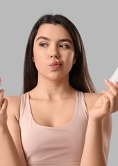 Nachdenkliche Frau hält Spray und Deo-Stick in den Händen, unschlüssig bei der Wahl ihres Deos.