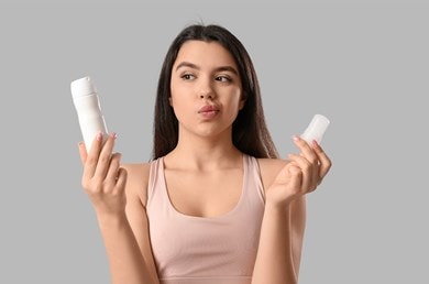 Nachdenkliche Frau hält Spray und Deo-Stick in den Händen, unschlüssig bei der Wahl ihres Deos.