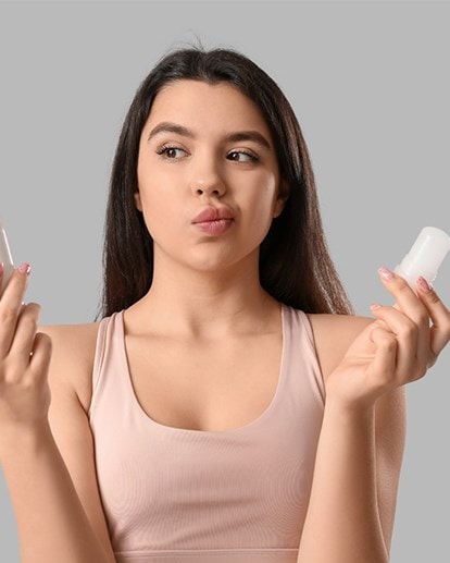 Nachdenkliche Frau hält Spray und Deo-Stick in den Händen, unschlüssig bei der Wahl ihres Deos.