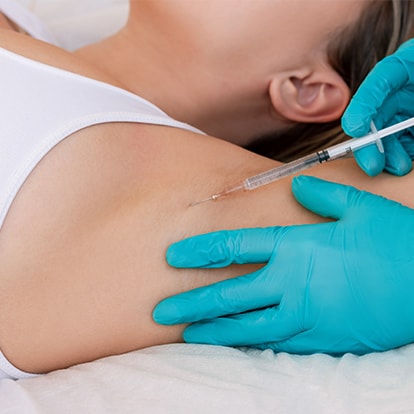 Arzt setzt eine Botox-Injektion in die Achsel einer liegenden Patientin 