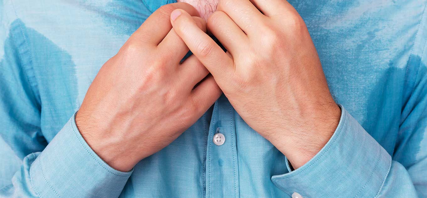 Mann mit schweissnassem Hemd im Brustbereich hält den Kragen mit beiden Händen fest