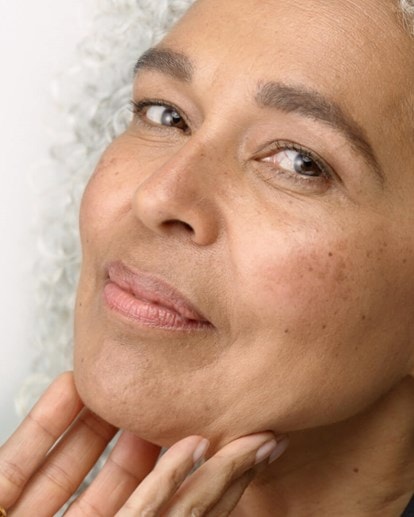 Frau mit grauem Haar lächelt leicht und streicht sich über die glatte, gepflegte Haut.