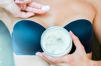 Frau zeigt cremige Sheabutter zwischen den Fingern über offenem Tiegel, reichhaltige natürliche Pflege für die Haut