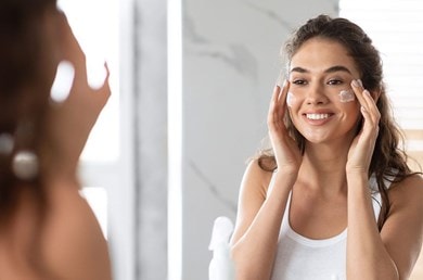 Lächelnde Frau pflegt ihr Gesicht mit Creme, Teil ihrer täglichen Hautpflegeroutine