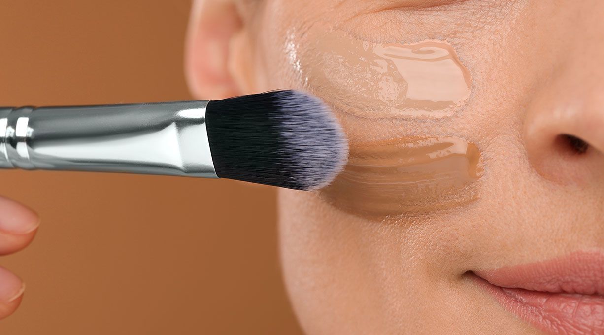 Pinsel verteilt flüssige Foundation auf Haut, sorgt für einen frischen, gleichmässigen Teint