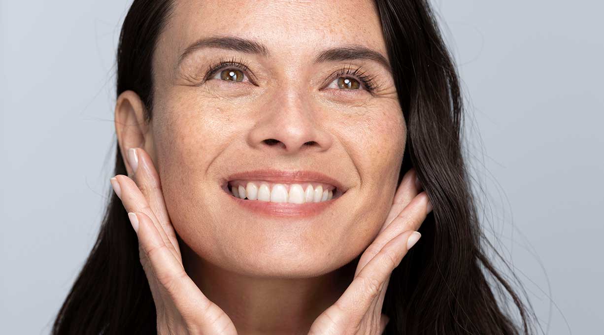 Strahlende Frau berührt sanft ihr Gesicht, glatte Haut durch pflegendes Gesichtsserum