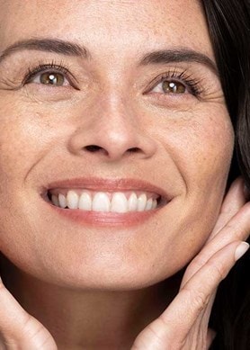 Strahlende Frau berührt sanft ihr Gesicht, glatte Haut durch pflegendes Gesichtsserum