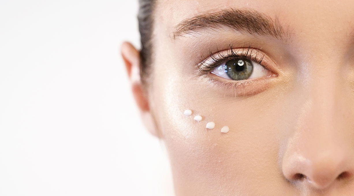 Eine Frau mit strahlend grünen Augen trägt sanft Augencreme unter ihren Augen auf.