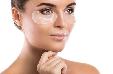 Nahaufnahme einer Frau mit Augenpads die ihr Kinn leicht berührt