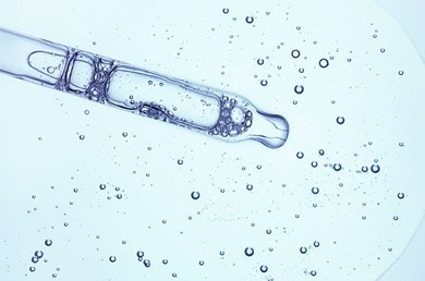 Nahaufnahme einer Pipette in einer transparenten Flüssigkeit mit Luftblasen, auf einem hellblauen Hintergrund.