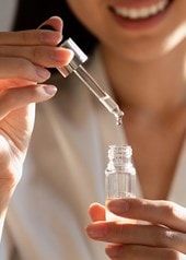 Une femme tient dans la main la pipette d'un flacon de sérum ouvert