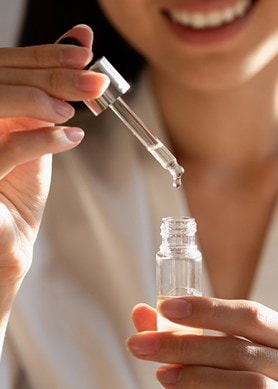 Une femme tient dans la main la pipette d'un flacon de sérum ouvert
