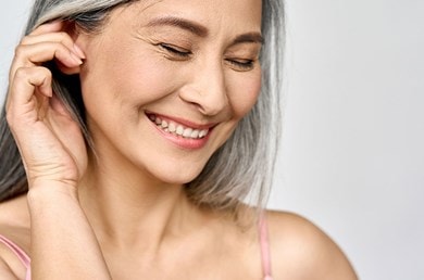 Ältere Frau mit grauen langen Haaren lächelt und schaut auf den Boden