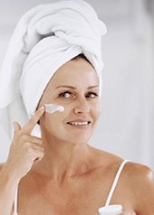 Frau mit Haarturban blickt in den Spiegel und cremt ihr Gesicht ein