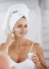 Frau mit Haarturban blickt in den Spiegel und cremt ihr Gesicht ein
