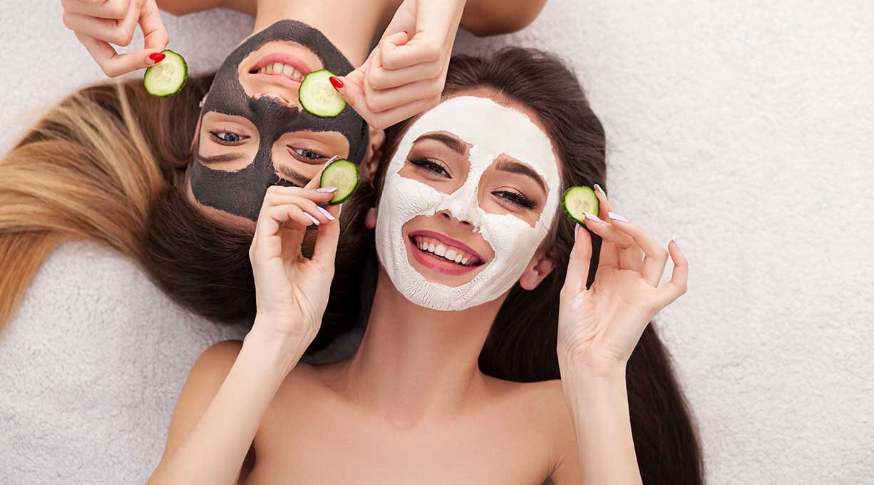 2 junge Frauen mit Gesichtsmasken und Gurkenscheiben in der Hand