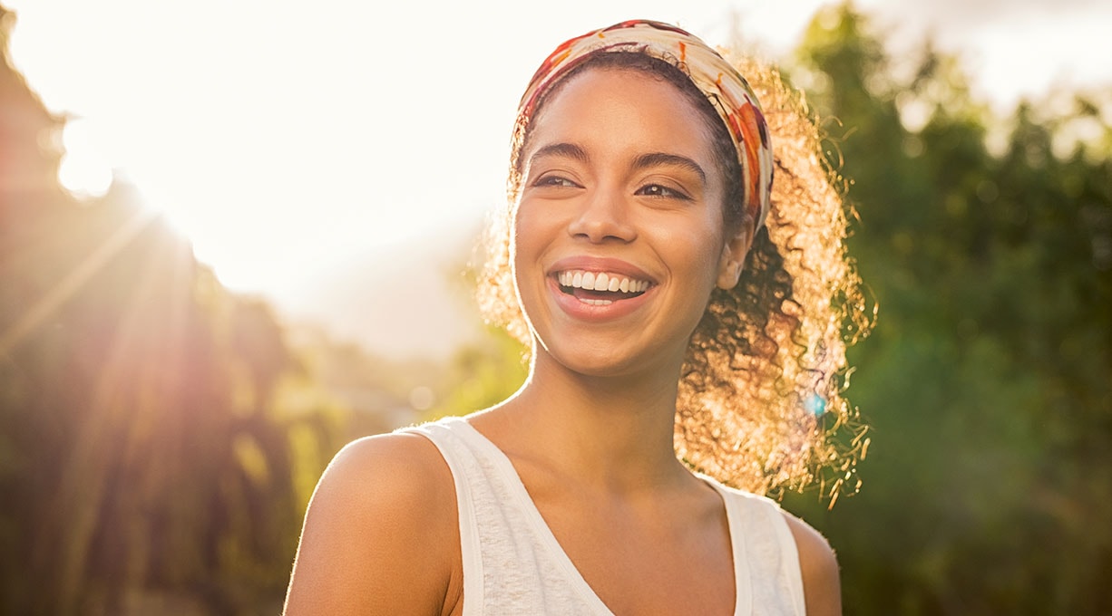 Junge Frau steht draußen in der Sonne und lacht