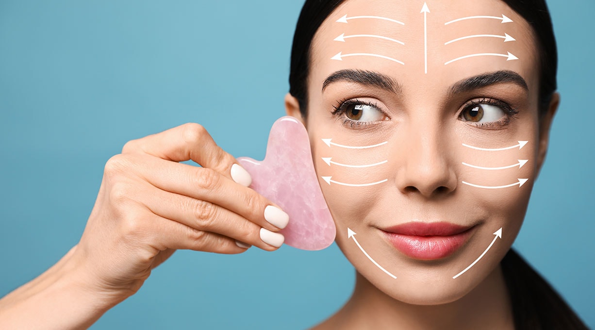 Eine Frau verwendet einen Gua Sha und fährt von außen nach innen über ihr Gesicht