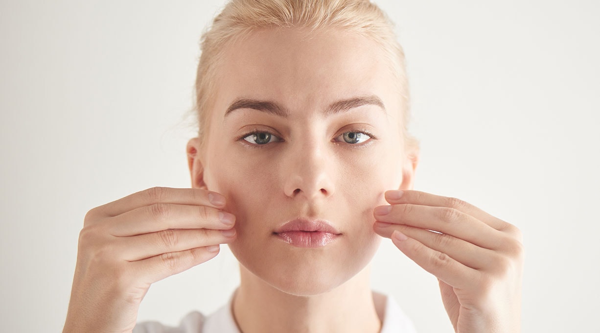 Eine blonde Frau berührt mit den Händen ihr Gesicht