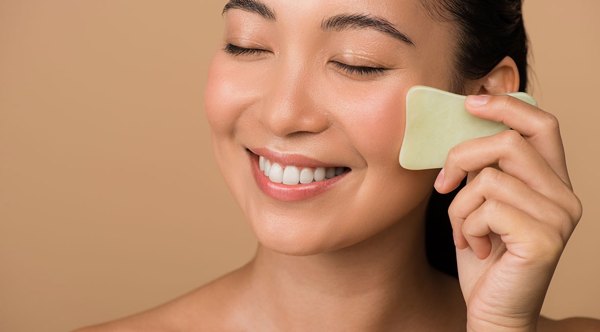 Eine Frau lächelt und hält einen Gua Sha an ihrem Gesicht