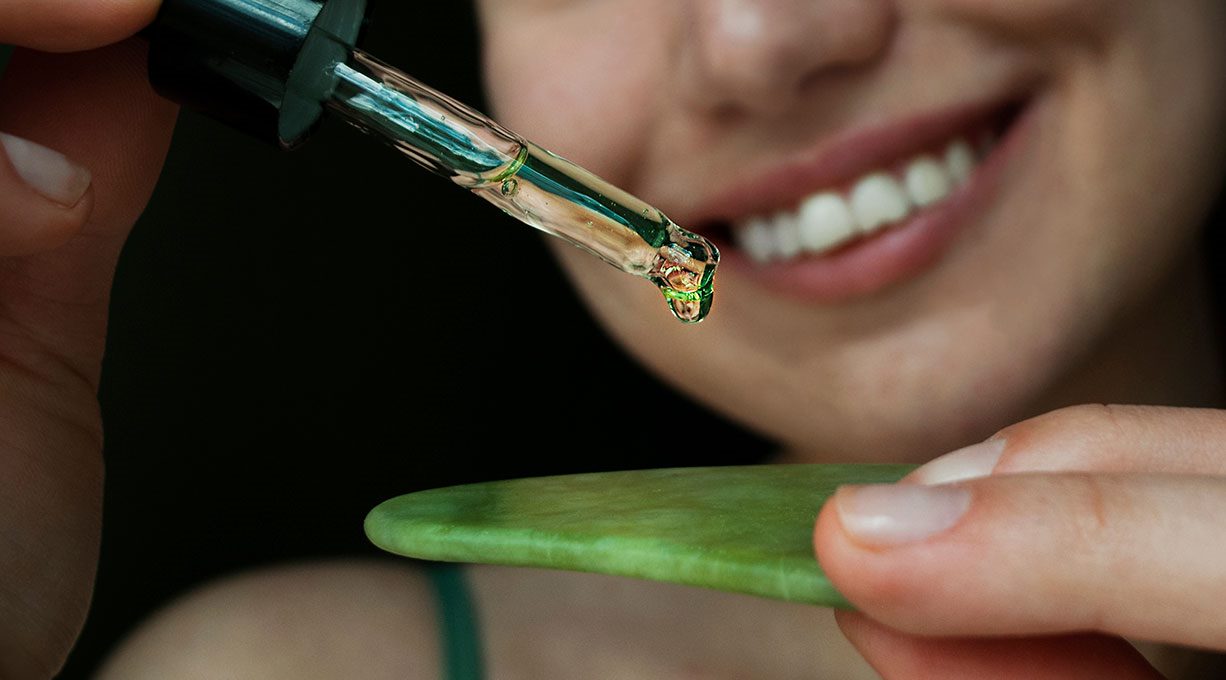 Frau tropft Gesichtsserum aus einer Pipette auf ein Gua Sha Tool