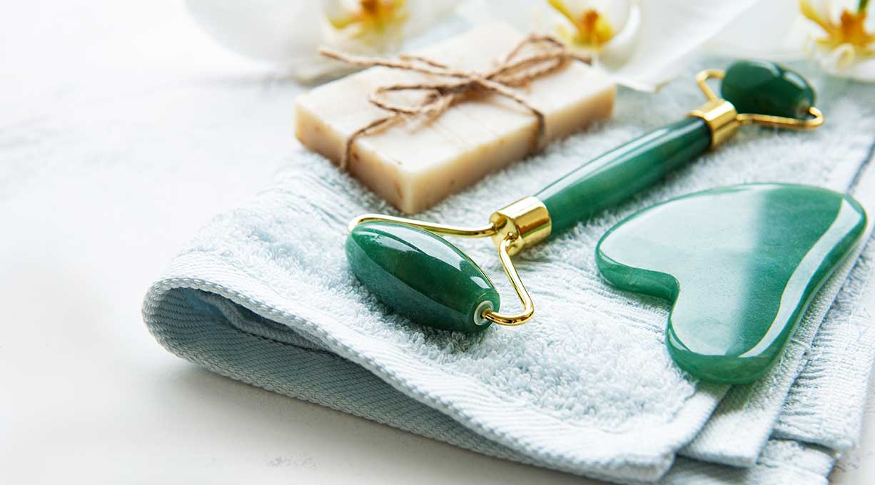 Ein Gua Sha liegt neben einem Roller und einem Stück Seife auf einem Handtuch