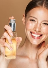 Junge Frau berührt lächelnd ihr Gesicht und hält ein Reinigungsöl in der Hand