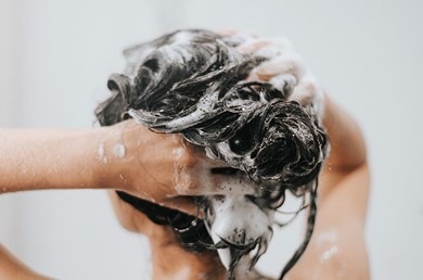 Eine Frau wäscht sich mit Shampoo unter der Dusche die Haare.