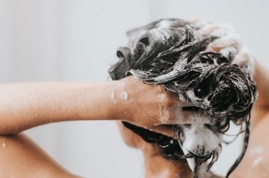 Femme sous la douche se lavant les cheveux avec un shampooing antipelliculaire.