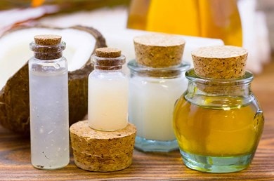 Mehrere kleine Glasflaschen mit Korkverschluss, gefüllt mit verschiedenen Ölen und Flüssigkeiten, neben einer aufgeschnittenen Kokosnuss.