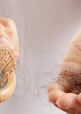 Nahaufnahme einer Haarbürste mit ausgefallenen Haaren in der Hand