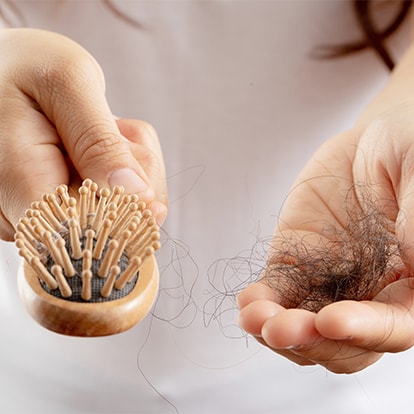 Nahaufnahme einer Haarbürste mit ausgefallenen Haaren in der Hand