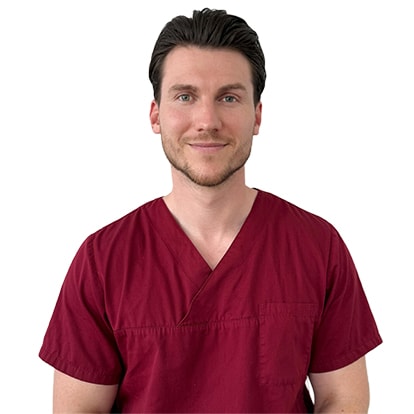 Dr Rouben Czwikla, vêtu d'une blouse médicale rouge foncé, regarde directement la caméra.