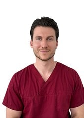 Dr Rouben Czwikla, vêtu d'une blouse médicale rouge foncé