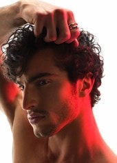 Männliches Model mit braunen Locken greift sich in sein Haar und zeigt sein Seitenprofil